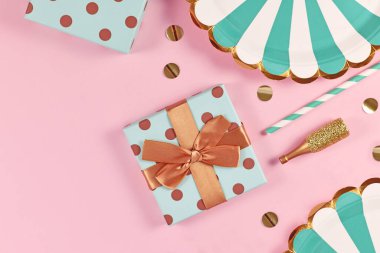 Mavi kağıt tabaklar, hediye kutuları, küçük altın şampanya şişeleri ve pembe arka planda konfetileri olan parti dairesi.