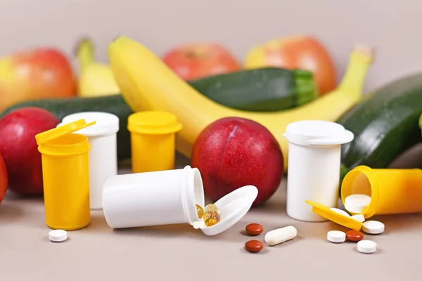 Capsules and pills of food nutrition supplements  with plastic bottles in front of fruits and vegetables in background