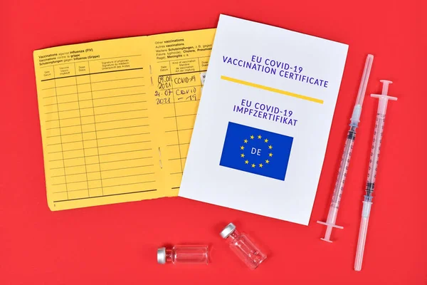 EU COVID-19 Vaccination certificate on paper, vaccine passport and syringes with vials on red background