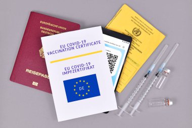 Almanya - Temmuz 2021: AB COVID-19 Aşı sertifikası kağıt ve dijital telefon, aşı pasaportu, seyahat kimliği ve gri arka plan üzerinde şişelerle birlikte şırıngalar