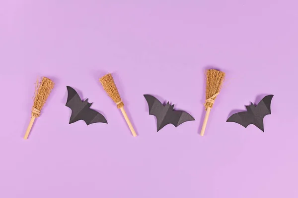 一排排紫色背景的万圣节纸制蝙蝠和女巫扫帚 — 图库照片