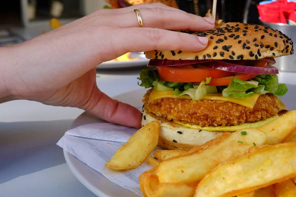 Mujer usando la mano para recoger una hamburguesa de ternera con papas fritas, curry, lechuga, tomate y cebolla —  Fotos de Stock