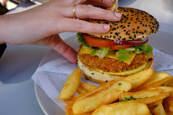 Mujer usando la mano para recoger una hamburguesa de ternera con papas fritas, curry, lechuga, tomate y cebolla —  Fotos de Stock