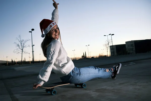 Jonge vrouw zitten op een skateboard met een kerstman hoed — Stockfoto