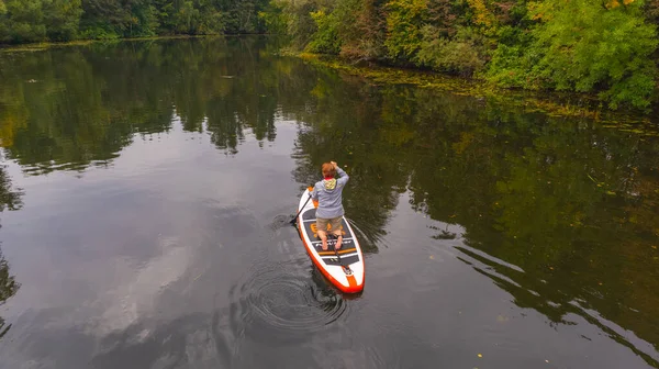 An elderly woman on a surfboard swims on the lake. Autumn. — Fotografia de Stock