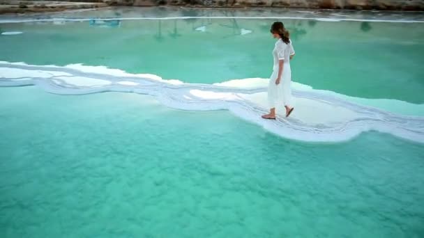 A girl in a white dress crossing the sea девушка в длинном белом платье идет по морской соляной косе — стокове відео