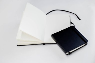 Beyaz sayfalar ve kurdele yer imlerine sahip küçük siyah, kapalı ve geniş defterler beyaz arkaplanda açılır.