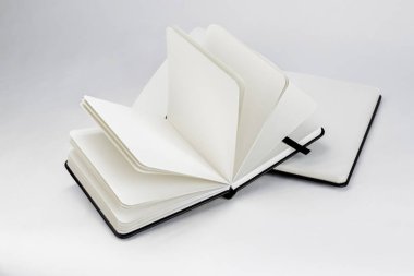 Boş beyaz sayfaları ve koyu renk kurdeleleri olan iki siyah yeni defter beyaz bir zemin üzerine serili.