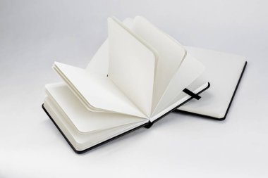 Two black open new notebooks with blank white pages and dark ribbons bookmarks lie unfold on a white backdrop clipart
