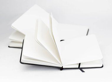 Two black open new notebooks with blank white pages and dark ribbons bookmarks lie unfold on a white background clipart