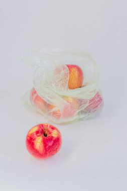 Şeffaf plastik buruşuk selofan poşet ve beyaz arka planda olgun kırmızı elmalar. Ekoloji kavramı