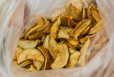 Beyaz arka planda, şeffaf plastik buruşuk selofan poşetteki sarı kurutulmuş elma dilimleri. Kuru meyve çerezi. 