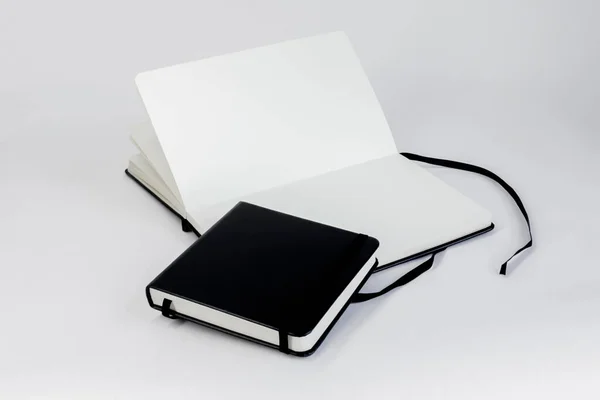 黒のノート2枚 小さな閉じた正方形のノートパッドは 空白の白いページと暗いリボンのブックマークを持つ大規模なオープン展開ノートブックに嘘 — ストック写真