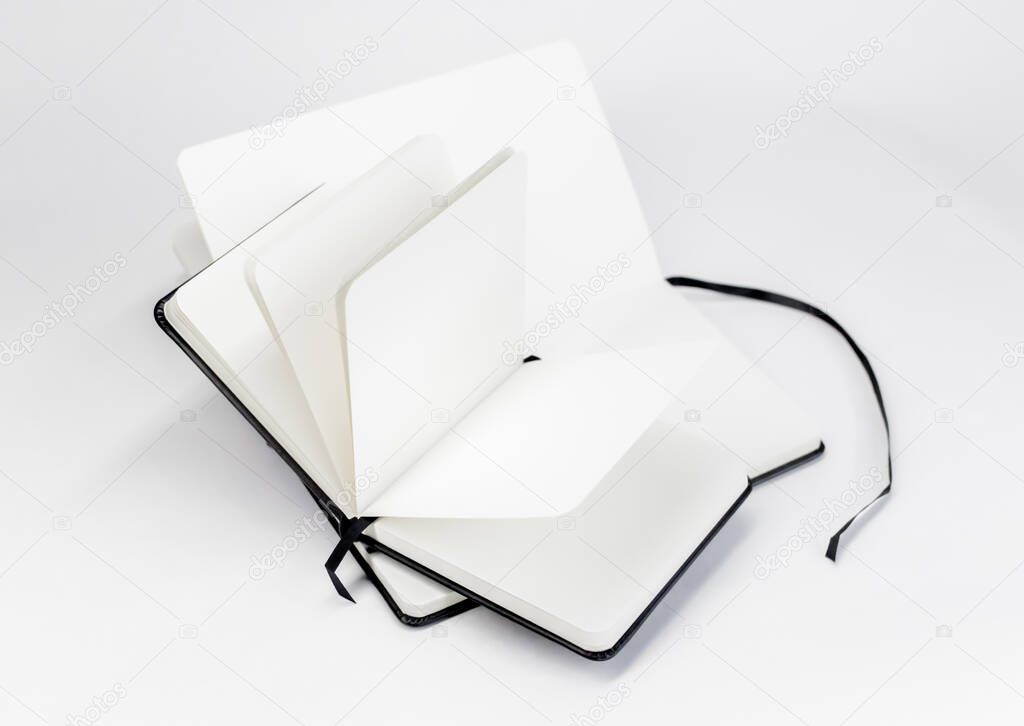Two black unfold open notebooks with blank white pages and dark ribbons bookmarks. Minimalistic background