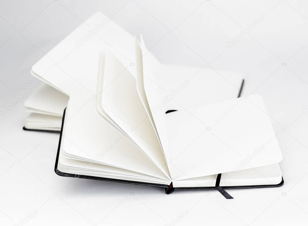 Two black open new notebooks with blank white pages and dark ribbons bookmarks lie unfold on a white background
