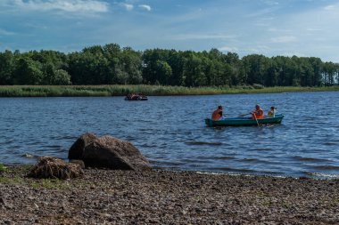Baltık Denizi 'nin körfezinde iki küçük yolcu kürekli sandalları yüzüyor. Yeşil ağaçların arasında, güneşli havalarda ormanlar. Taşlar sahili. Rusya yazı
