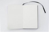 Rozbalte otevřený notebook, knihu s prázdnými bílými stránkami a černou stuhou, záložku na světlém pozadí. Skicák. Horní pohled