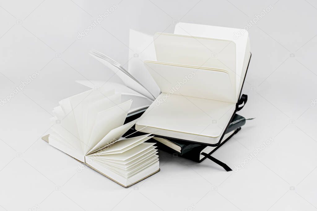 Unfold notebooks lie on top of each other. Fan open notepads with blank light beige pages. White backdrop.