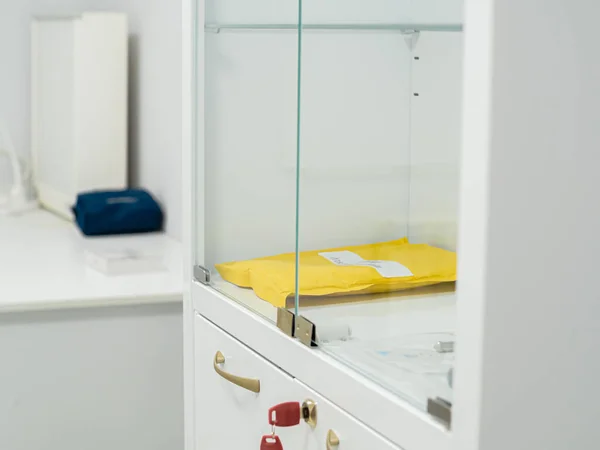 Kapalı cam kapıların arkasındaki sarı klasörlü yeni beyaz dolap. Çekmecenin kilidine kırmızı anahtar yerleştirdim. Minimalist hafif dolap. Tıbbi oda. Yakın plan.