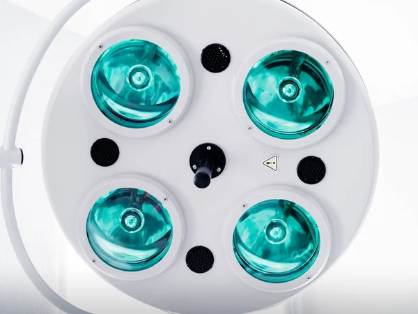 Round white swivel medical operating lamp with four green blue turquoise lights and black details in doctor\'s office