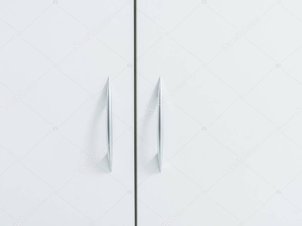 White cabinet doors with thin metal handles. Minimalistic light cupboard. Close-up