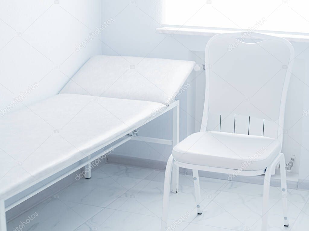 White chair and medical couch for examining and treating a patient  in light clean doctor's office. Workplace