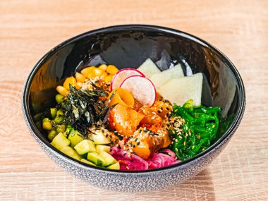 Somon, avokado, turp, mısır, yosun, bezelye, nori, daikon, susam tohumu. Kafede, restoranda, ahşap bir masada, siyah seramili Asya yemekleri.