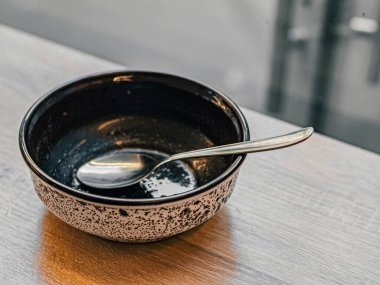 İçinde metal kaşık olan bir yemekten sonra boş kirli tabak pencerenin yanındaki ahşap bir masada duruyor. Siyah beyaz çorba tabağı