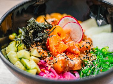 Somon, avokado, turp, mısır, yosun, bezelye, nori, daikon, susam tohumu. Kafede, restoranda, siyah tabakta lezzetli Asya yemekleri. Yakın plan.