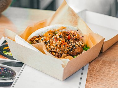 Karton kutuda tavuklu bao. Etli pirinç çörekleri, sosla doldurulmuş sebzeler, susam tohumlarıyla serpiştirilmiş. Bir kafede menü, restoran. 