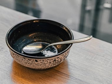 Yemekten sonra boş kirli tabağın içindeki metal kaşık pencerenin yanındaki ahşap masada duruyor. Siyah beyaz çorba tabağı