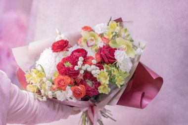 Bir buket kırmızı, turuncu, sarı, beyaz, narin çiçekler farklı boyutlarda ve renklerde, güller, kadının elinde yeşil yapraklar. Kağıt ambalaj. Aşk..