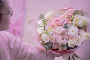 Bir kadın elinde açık pembe, beyaz, narin, farklı boyutlarda küçük güller, yeşil yapraklardan çiçekler tutuyor. Kağıt ambalaj. Aşk..