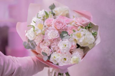 Bir el açık pembe, beyaz, narin, farklı boyutlarda küçük güller, yeşil yapraklardan çiçekler tutar. Kağıt ambalaj. Aşk..
