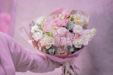 A lush bouquet of light pink, white cute delicate small roses of different sizes, flowers of green leaves in hand of woman. Paper packaging. Romance.