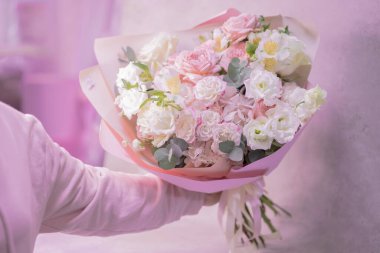 Bir adamın eli, açık pembe, beyaz, farklı boyutlarda küçük güller, yeşil yapraklardan çiçekler, güzel bir buket çiçek tutar. Aşk..