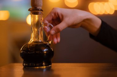 Kıvırcık şişe, cam mantarlı ince boyunlu, balzamik sirkeli, yağlı, elinde sos olan bir adam, kadın. İtalyan mutfağı, kafe, restoran, sıcak bulanık arka plan.