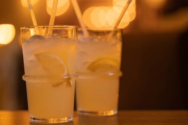 İki bardak limonata, limon dilimleri, buz küpleri, pipetler. Yaz nezlesi ferahlatıcı alkollü kokteyl, bir kafedeki ahşap masada içmek, bar. Yakın plan. Metin için yer