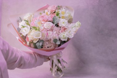 Açık pembe bir buket, farklı boyutlarda beyaz, narin küçük güller, bir kadının elinde yeşil yapraklardan çiçekler. Kağıt ambalaj. Romantizm. Metin için yer