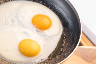 Hafif pişmiş, yumuşak yumurta ve kenarları beyaz, iki yuvarlak çiğ yumurta, siyah bir tavada çatlaklar. Güneş ışığında basit bir kahvaltı. Üst görünüm, yakın çekim