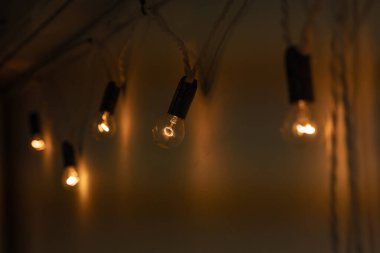 Yuvarlak küçük ampuller, beyaz bir duvarda asılı sıcak turuncu ışık ile parlıyordu. Karanlık bir odada tavan arası dekorasyonu. Ampuller birbirine bir çelenk gibi bağlıdır. Yakın plan.