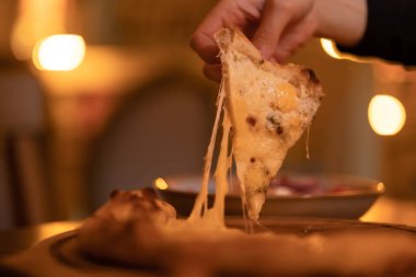 Bir kadının eli bir dilim sıcak vejetaryen dört peynirli pizzayı yakın plan peynirli, sıcak akşam ışığı ile alır. Restoranda yeni hazırlanmış İtalyan yemeği, kafe.