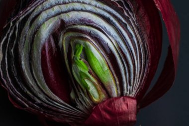 Kırmızı filizlenmiş soğanları siyah bir tabakta ikiye böl. Yan görüş. Derin renklere sahip kavramsal makro fotoğrafçılık