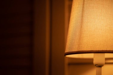 Basit bir abajuru olan küçük, rahat bir masa lambası. Akşamları yayılmış, sakin, sıcak bir ışık. İç mekanda minimalizm ve konfor. Yakın plan.