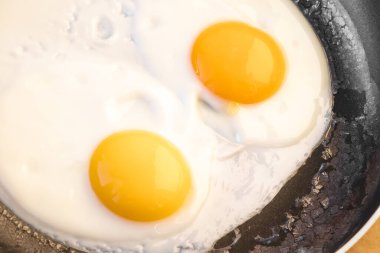 Kızartma tavasında kenarlarında çatlaklar olan iki parlak, çiğ yumurta sarısı. Yumuşak, yumuşak yumurta pişirmek basit bir yemektir. Üst görünüm