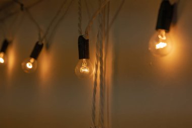 Siyah tabanlı yuvarlak küçük ampullü çelenkler ve karanlık bir odada beyaz bir duvara asılı sıcak turuncu ışık. Çatı katı tarzı dekor. Yakın plan. İyi akşamlar.