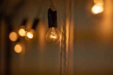 Yuvarlak küçük ampul, beyaz bir duvarda asılı sıcak turuncu ışık ile parlıyordu. Çatı katı tarzı dekor. Ampuller birbirine bir çelenk gibi bağlıdır. Yakın plan, bokeh bulanık arkaplan