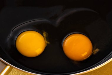 Siyah gümüş bir tavada şeffaf beyazlar içinde iki ham parlak yuvarlak yumurta sarısı kahvaltı için basit bir yemek pişirme süreci konsepti. Sıcacık. Üst görünüm