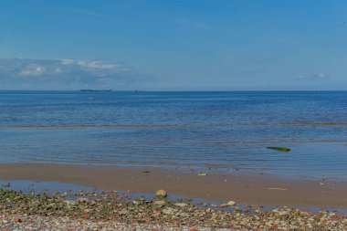 Kuzey Baltık Denizi 'nin kumlu çakıl taşı kıyısı. Yeşil ve kırmızı taşlar, bulutlu mavi gökyüzü.
