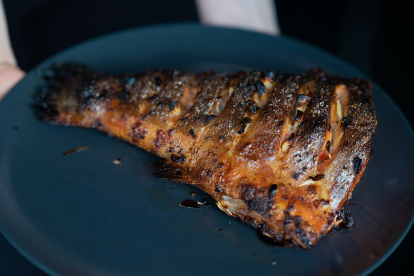 Very appetizing and delicious cooked salmon tail on a dark plate. Grilling recipes. Macro photo of food